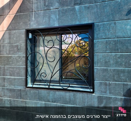 חלון עם מסגרת ברזל מעוצבת על קיר אבן אפור